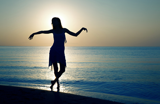 Silhouette of the woman doing relaxing dance exercise at the beach during sunset. Natural darnkess and colors