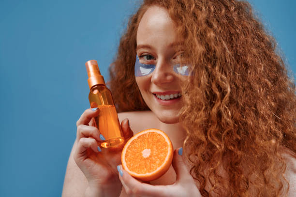 Redhead girl with freckles on a blue background Beautiful redhead plus size woman with freckles using eye patches and holding serum oil with orange isolated on blue background. Body positive. Cosmetology and skin care. oranges with faces stock pictures, royalty-free photos & images