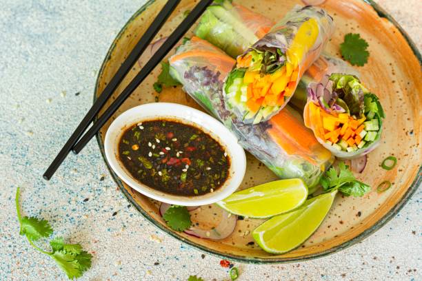 istock Fresh Asian appetizer Spring rolls (Nem) made from rice paper and raw vegetables and herbs with hot sauce on a light blue background. 1497629610