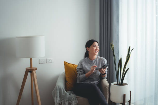 Asian woman happy smiling sitting on armchair using smart phone and credit card for shopping online at home. Asian woman sitting on armchair in living room using smart phone and credit card for shopping online at home. Happy woman shopper using instant mobile payments making purchase in online store. types of loans stock pictures, royalty-free photos & images