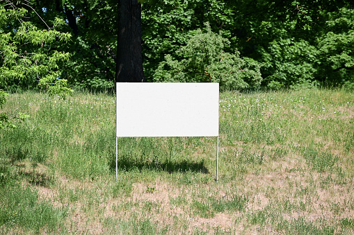 White board set on the ground with green grass against the background of trees and bushes outside on a summer day