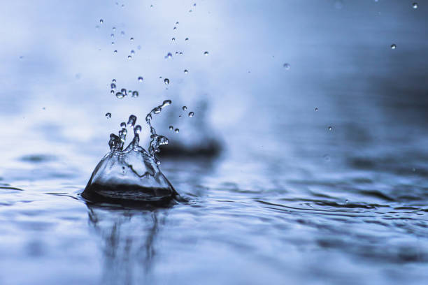 Water rain droplet forming splash crown in turquoise blue water in sparkling light