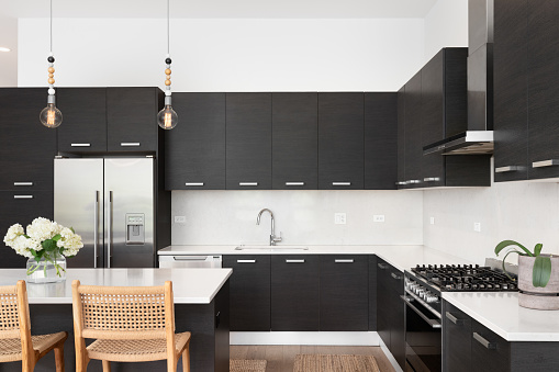 A beautiful kitchen with dark wood cabinets, marble countertops, chairs sitting at the island, and stainless steel appliances. No brands or names.