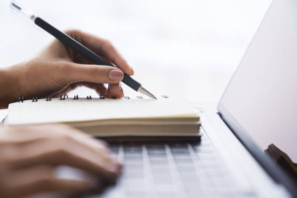 istock In close view, a woman's hand writing down notes in a notepad on a laptop, against a hazy backdrop 1497641709