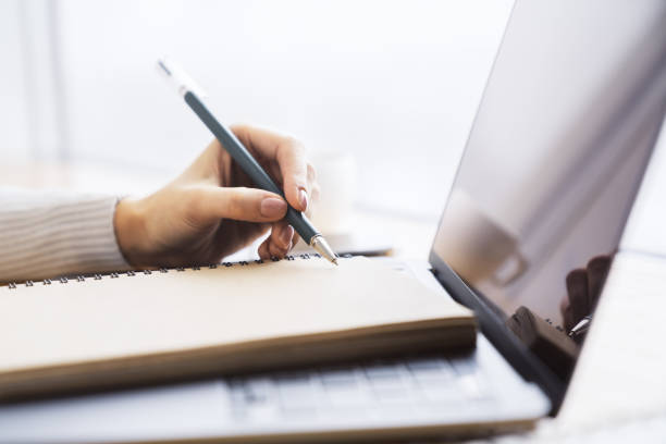 istock Close perspective of a woman's hand making entries in a notepad on a cutting-edge laptop, with a soft blur in the surrounding 1497641746