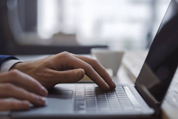 Against a fuzzy office backdrop, a close-up captures a man's hands deftly navigating a modern laptop's keyboard.