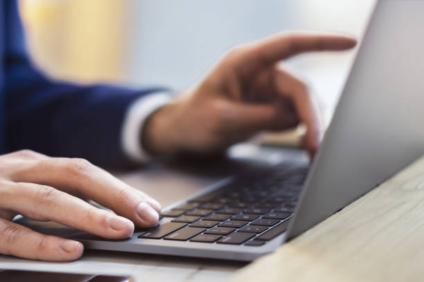 クローズアップショットでは、男性の手が最先端のラップトップのキーボードで入力しているのが見られ、背景にはオフィスシーンがそっとぼやけています。 - mail keyboard button ストックフォトと画像