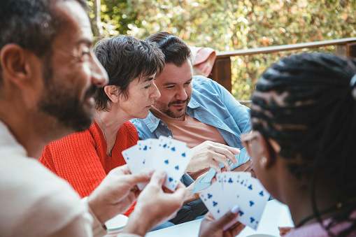 Close up on Diverse People playing cards together around the table on a terrace
