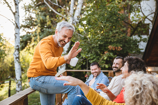 Mature people enjoying in a home garden, smiling and relaxing. Friends talking jokes and give five for good mood. Copy space