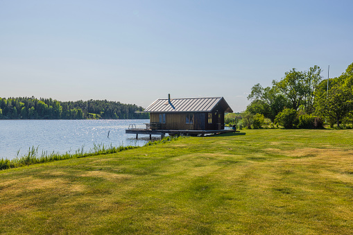 Beautiful view of small utility house on lake on blue sky background. Sweden, Europe.