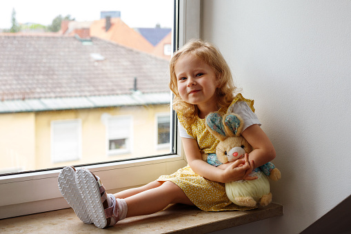 little girl with a soft toy on the window preschool