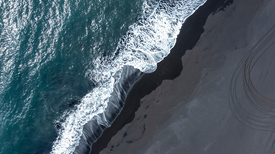 Breathtaking aerial view of nature, cold ocean and strong waves lapping the black sand beach