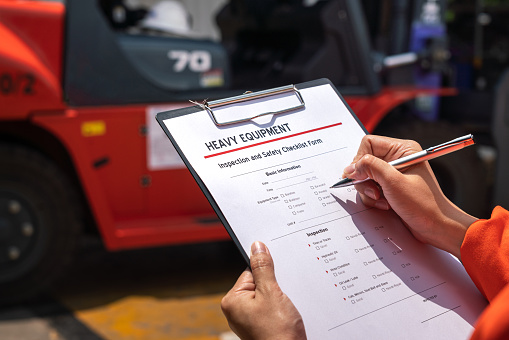 A mechanical engineer is using heavy equipment checklist form for inspecting the factory forklift vehicle (as blurred background). Industrial working with safety practice concept, selective focus.