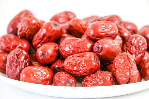 Close up of lots of sweet red Jujube dates (also known as Ziziphus jujube, Chinese dates) on a white plate on white table