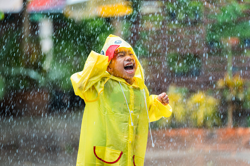 Asian boy wearing a raincoat outside the house. He is playing in the rain.