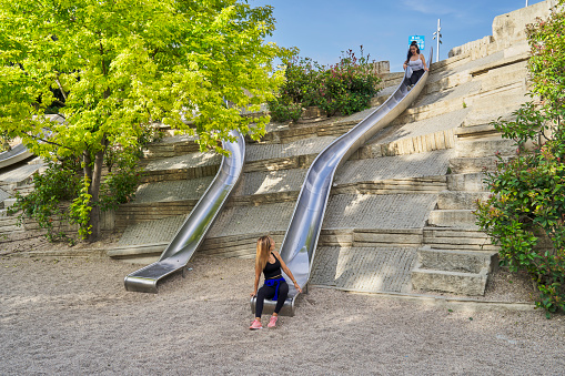 A COUPLE OF GIRLS IN SPORTS CLOTHES JUMPING DOWN A SLIDE IN AN OUTDOOR PARK