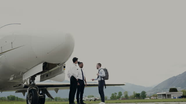 Business man boarding private plane, pilots greeting him