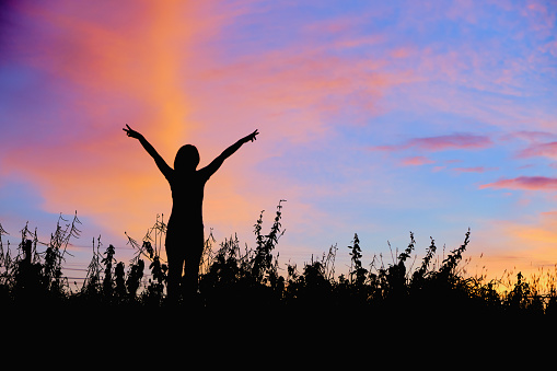 Silhouette of women with hands up Against the sunrise background