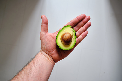 Man holds a green cut avocado in her hands. Avocado close-up. Natural fresh organic exotic fruits. Healthy food, raw food diet. Vegetarian life. Proper nutrition. Ready to eat. Eco product. Poster