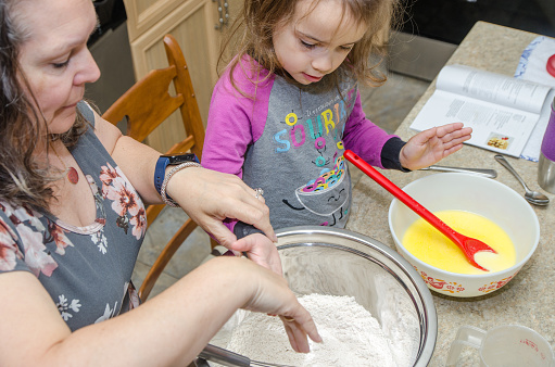 Grandmother and granddaughter preparing waffle dough on the kitchen counter during day