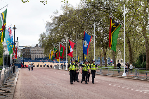 A contingent of police officers from South Wales police force walking along Spring Gardens towards The Mall to help control crowds at the imminent Changing of the Guard which takes place daily. They had been on duty in London for the Coronation of King Charles III. Spring Gardens is lined with flags of Commonwealth countries and Horse Guards Parade is in the distance.