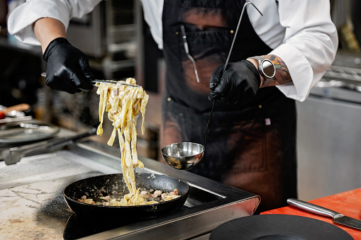 Close-up of male chef preparing pasta carbonara in restaurant kitchen