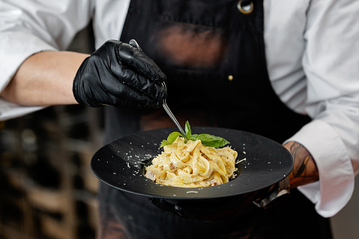 Close up of concentrated chef finishing a pasta carbonara dish in restaurant kitchen
