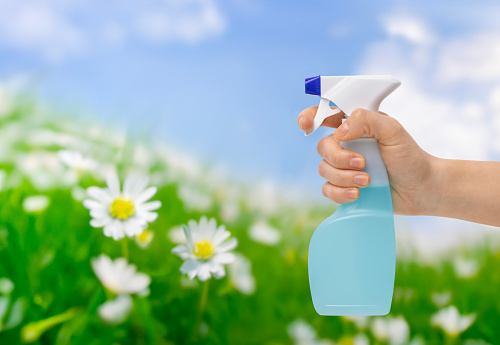 Woman's hand sprays with a light blue cleaning bottle in front of a blurred green nature landscape background