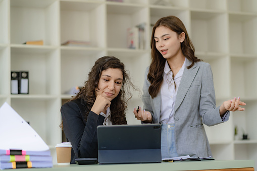 Businesswoman and accountant talking with laptop and tablet Two attractive millennial caucasian businesswoman planning project together at table in office