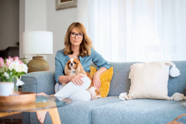 Full length of an attractive mid aged woman relaxing at home with her cute cavalier puppy stock photo