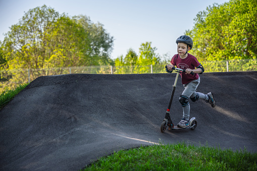 Boy riding push scooter at the outdoors pump track