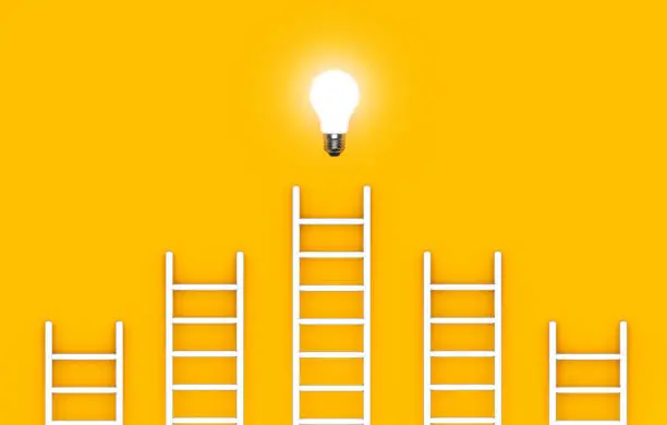 Photo of Ladder reaches up to a lit light bulb representing an Idea, creativity, invention concept.