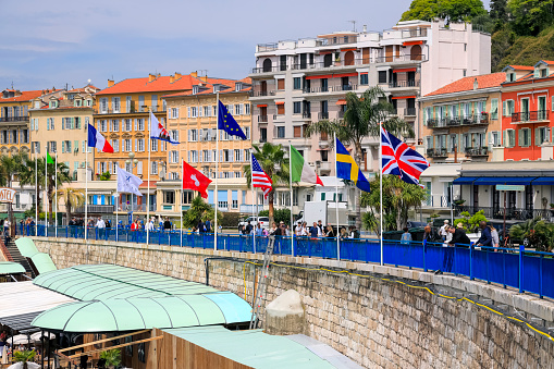Nice, France - April 22, 2023: Residential houses on the seafront promenade. Various flags fly on the masts. You can see people walking along the promenade