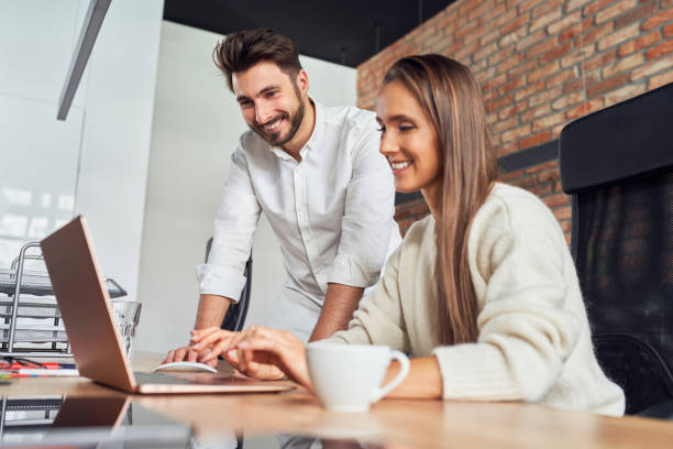 Two business people talking in office using laptop working together stock photo