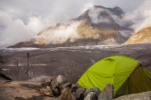 In the Swiss mountains, a tent and tripod overlook the Aletsch Glacier and Olmenhorn Mountain, creating a picturesque scene of adventure and serenity.