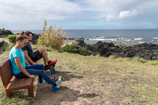 Two people on the bench having fun at the coastline near Escalvado towards the Mosteiros and the Ilhéus dos Mosteiros on Sao Miguel, Azores