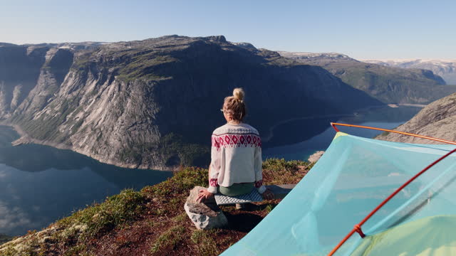 SLOW MOTION: Female hiker contemplating spectacular views from her tent, wild camping in Norway