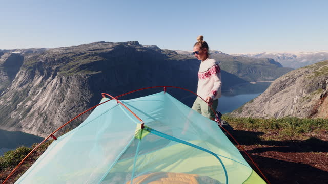 SLOW MOTION: Woman setting up tent outdoors in Norway, spectacular view
