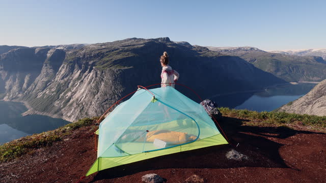 SLOW MOTION: Woman setting up tent outdoors in Norway, spectacular view