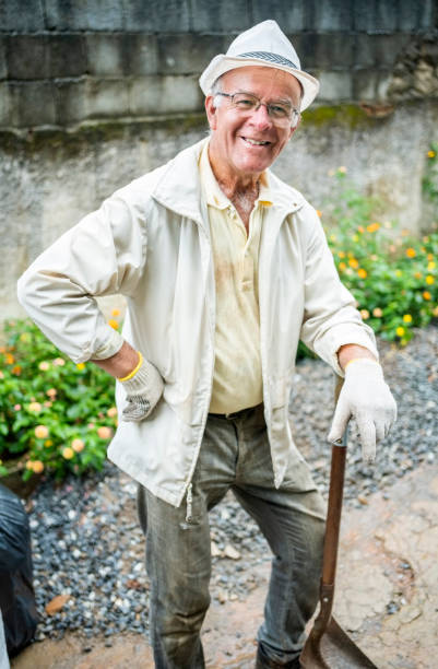 Portrait of a happy senior male volunteer with shovel standing outside during community cleaning up