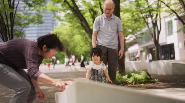 Grandparents are having fun and enjoying playing with their granddaughter in a public park in the city outdoors.