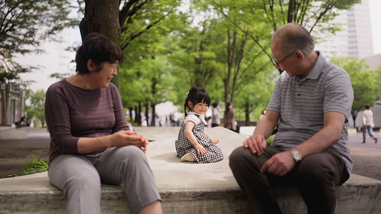 Grandparents are having fun and enjoying playing with their granddaughter in a public park in the city outdoors.