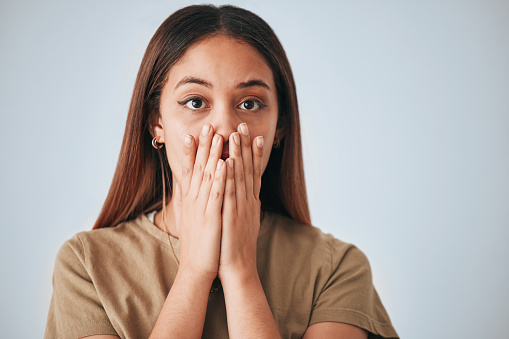 Portrait, woman and surprise in a studio with a female cover mouth from shock. Isolated, grey background and hands on a face of a young person model with wow, worry and alert reaction from secret