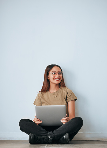 Laptop, student woman and smile by a wall with computer work for learning with happiness. University, college and house with floor sitting of a happy young person ready for studying with mockup