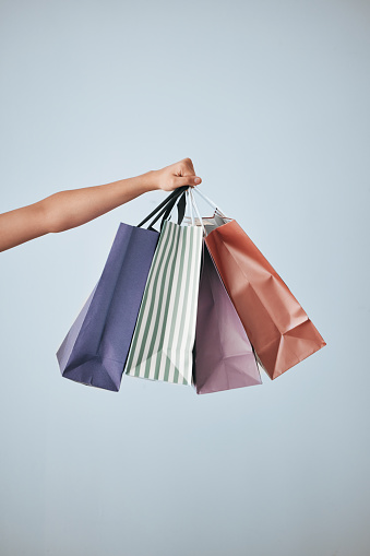 Hands, shopping bags and purchase on mockup in sale, discount or fashion against a gray studio background. Hand of shopper holding bag of gifts, present or luxury retail products on copy space