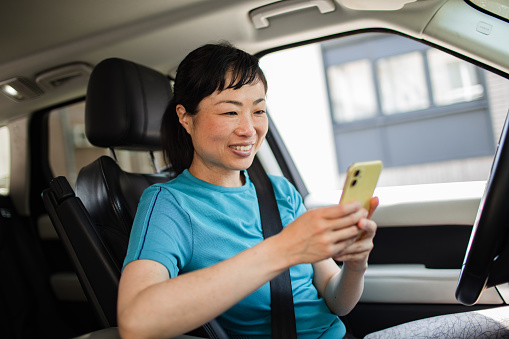 Close up of a Young Japanese woman driving a car and using a smart phone