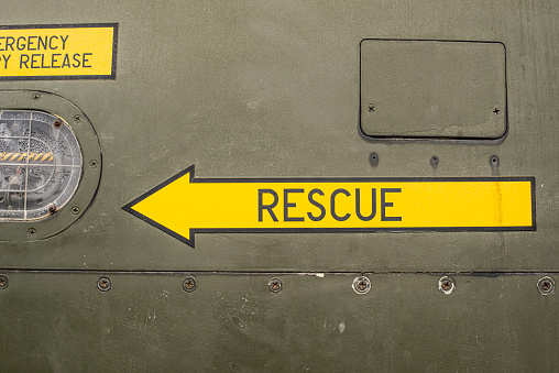 A yellow rescue arrow painted on to the side of a military green riveted metal panel.  Background texture.
