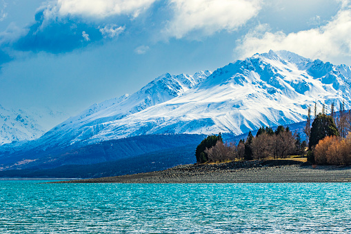 Turquoise lake with dramatic landscape of snow capped mountains in background, shot in New Zealand.