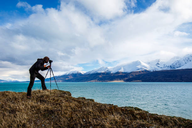 istock Young professional man operating camera equipment on tripod setup taking photographs of dramatic mountain landscape 1497731885