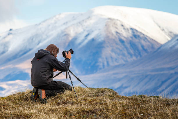 istock Young professional man operating camera equipment on tripod setup taking photographs of dramatic mountain landscape 1497731891